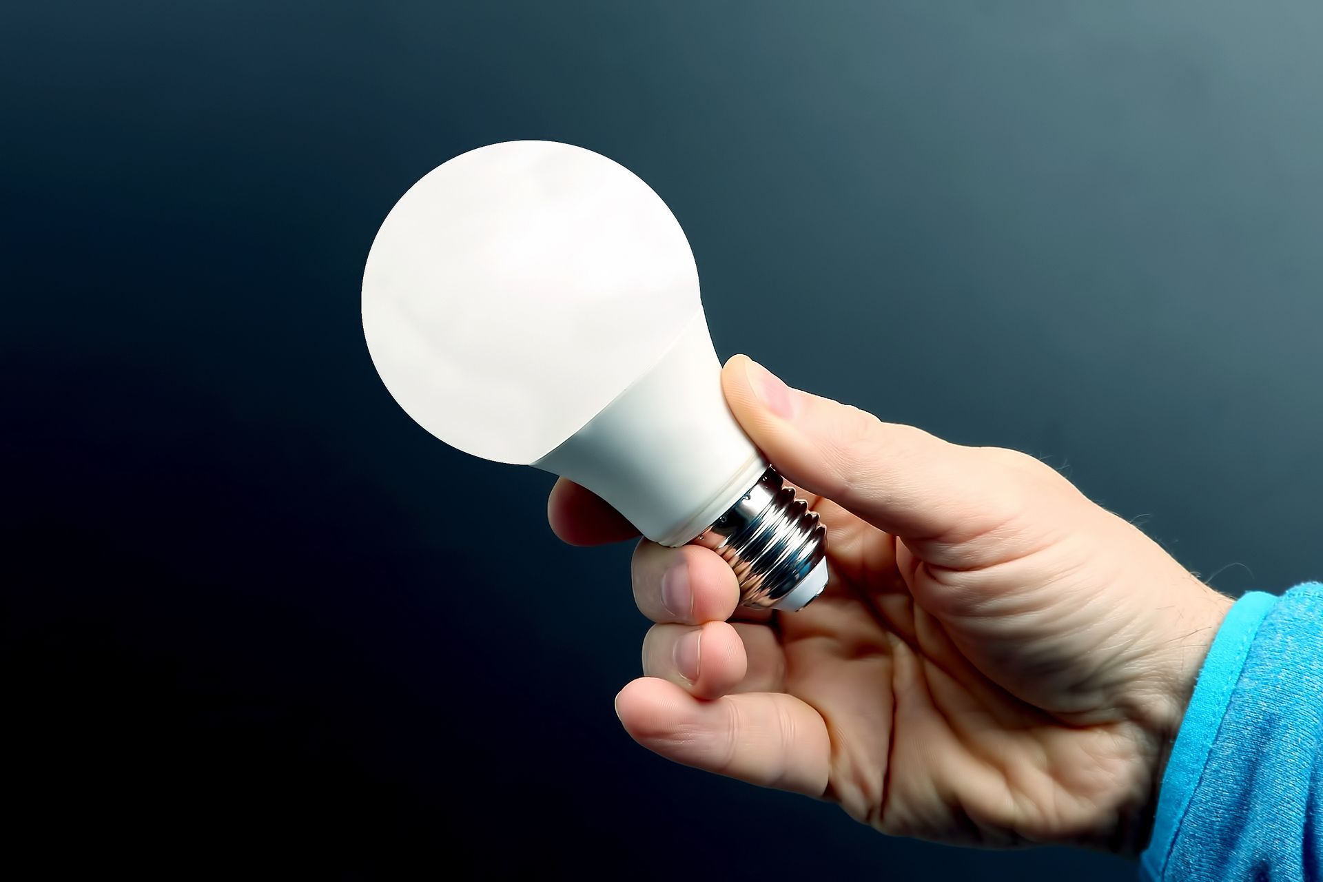 Hand holding a lit, round white LED lightbulb against a dark background.