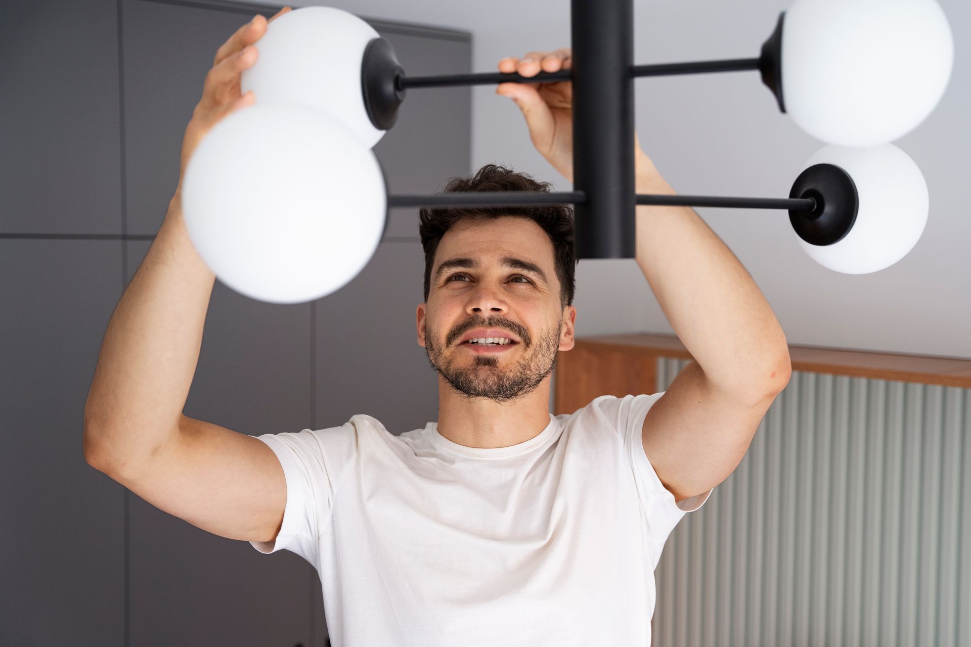 Man installing a modern black chandelier with white globe lights.