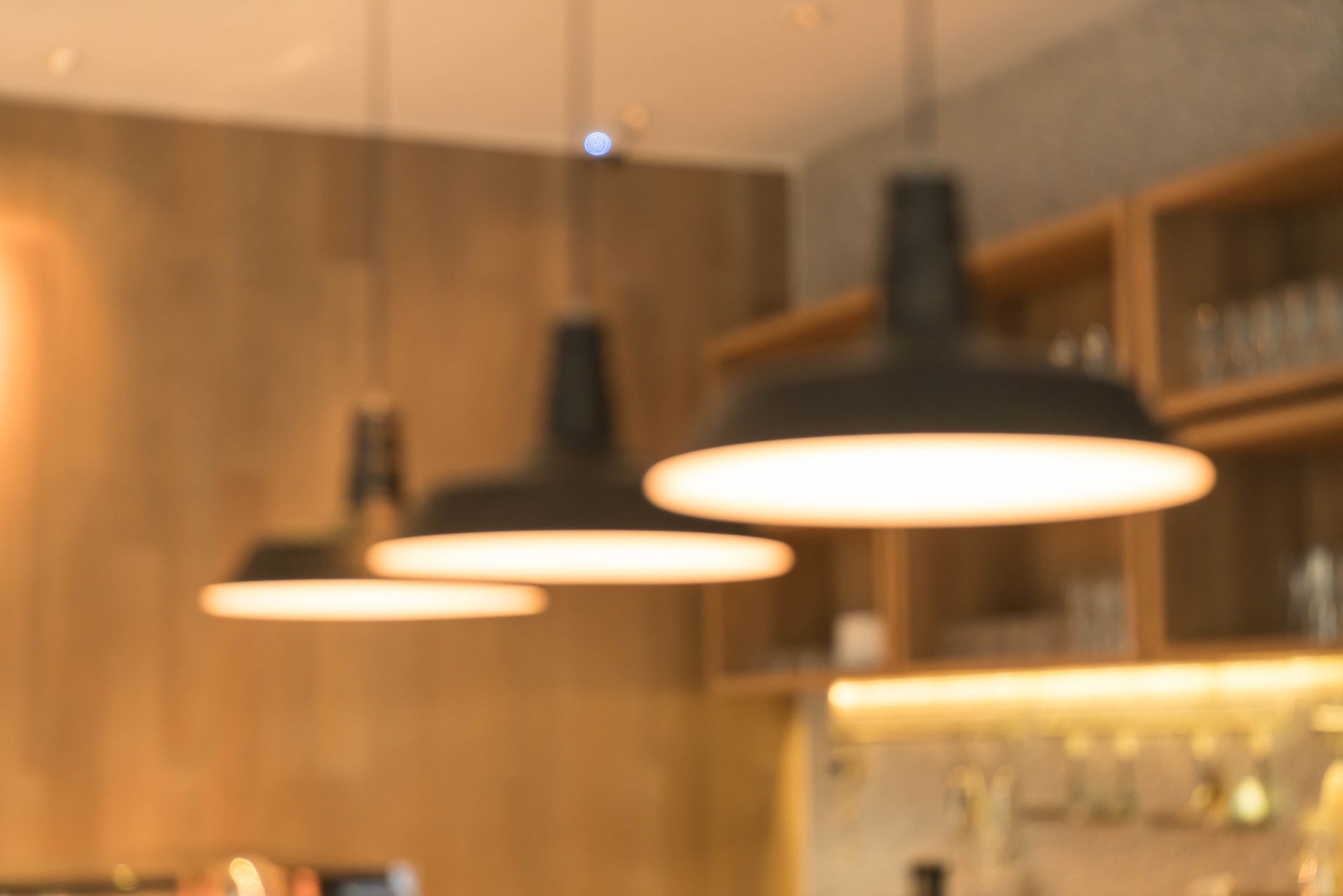 Three pendant lights hanging above a bar, with wooden shelves in the background.
