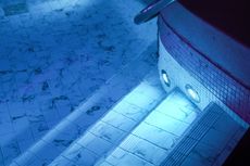 Blue-lit poolside deck beside a curved tiled pool at night, with underwater lights glowing.