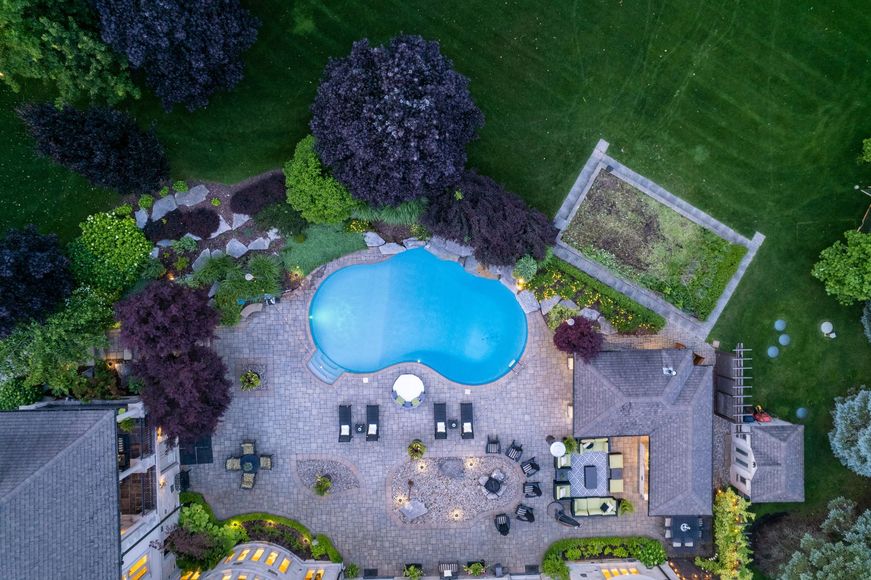 Aerial view of a backyard with a blue swimming pool, patio furniture, trees, and a small shed