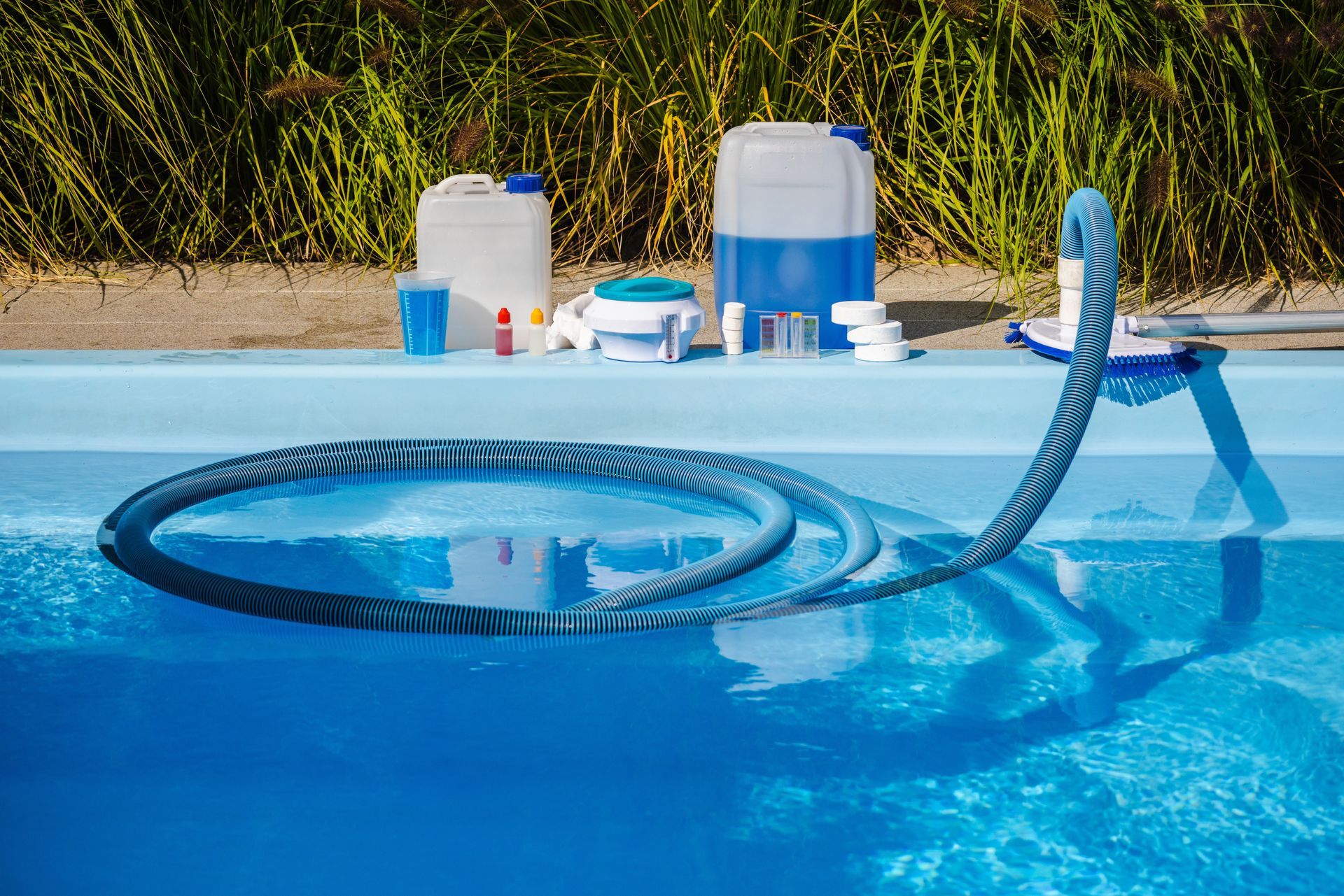 Blue pool vacuum hose coiled in a swimming pool beside cleaning supplies on the deck