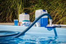 Pool vacuum hose and cleaning supplies beside a backyard swimming pool with blue water