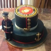 Marine Corps-themed cake with a toy Marine figurine, black and gold with red trim