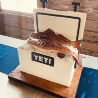 YETI cooler with fish mounted on top, displayed on a wooden base at a dockside setting