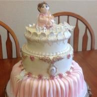 Decorative pink-and-white tiered cake with a small doll topper on a dining table