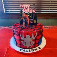 Spider-Man birthday cake with “Happy Birthday” topper and name “Callum” on a red table