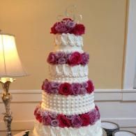 White tiered cake with pink rose decorations on a table indoors