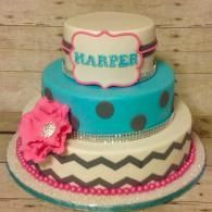 Three-tier turquoise and cream birthday cake with pink accents and “HARPER” topper