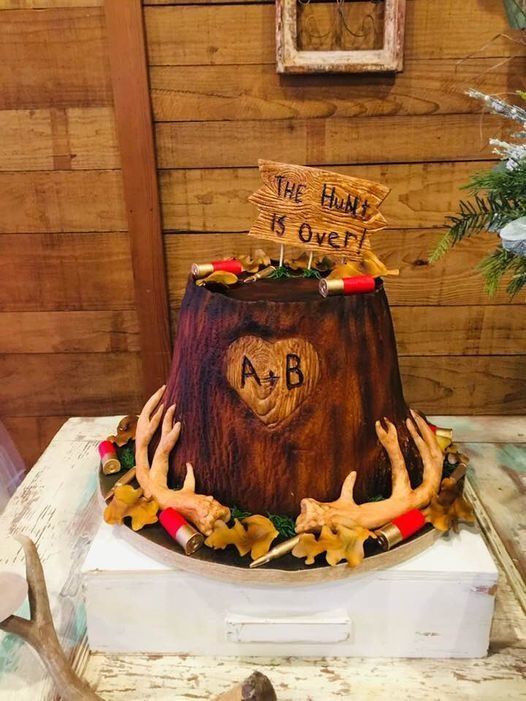 Woodland-themed cake with antlers, berries, and “A+B” on a wood-grain base, topped with “the hunt is over” sign