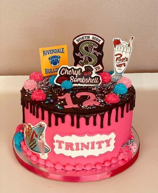 Pink and black birthday cake with “Trinity” plaque, number 12 topper, and colorful candy decorations