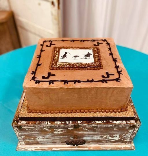 Decorated square brown cake on a vintage wooden box, with a small bird motif on top.