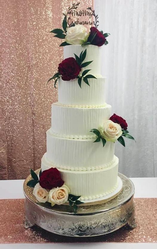 Three-tier white wedding cake with red and blush roses on a silver stand