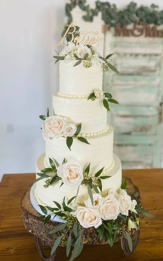 Tall white tiered wedding cake with cream roses and greenery on an ornate wooden stand