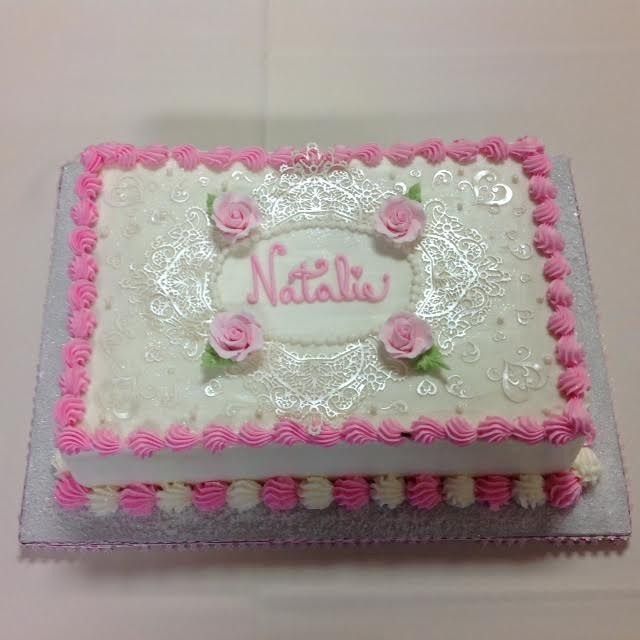 Pink and white decorated cake with “Natalie” written on top and small pink roses around it