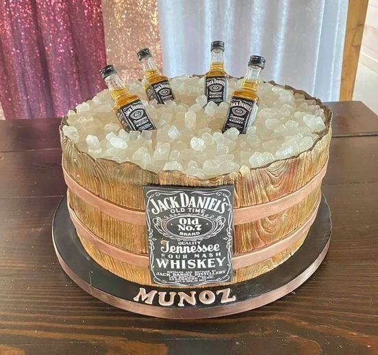 Jack Daniel’s whiskey barrel cake with ice cubes and three mini bottles on a table, labeled “MUNOZ.”