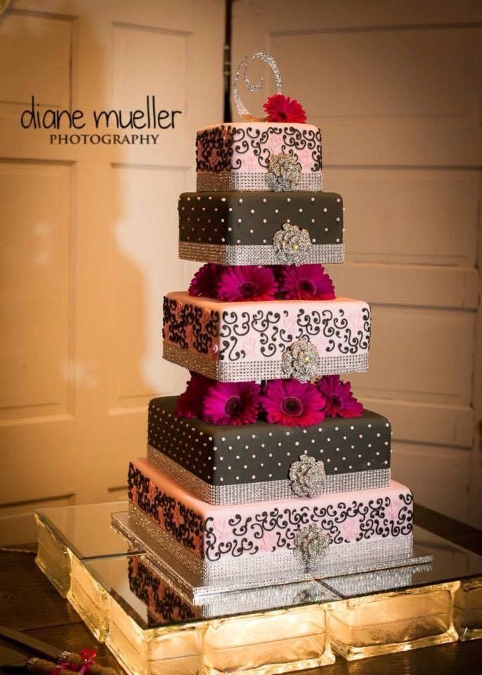 Five-tier wedding cake with white and dark patterned layers, topped with a red flower, on a mirrored stand