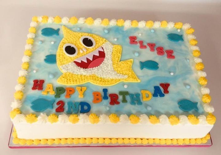Birthday cake with yellow shark decoration and “Happy Birthday” lettering on blue frosting