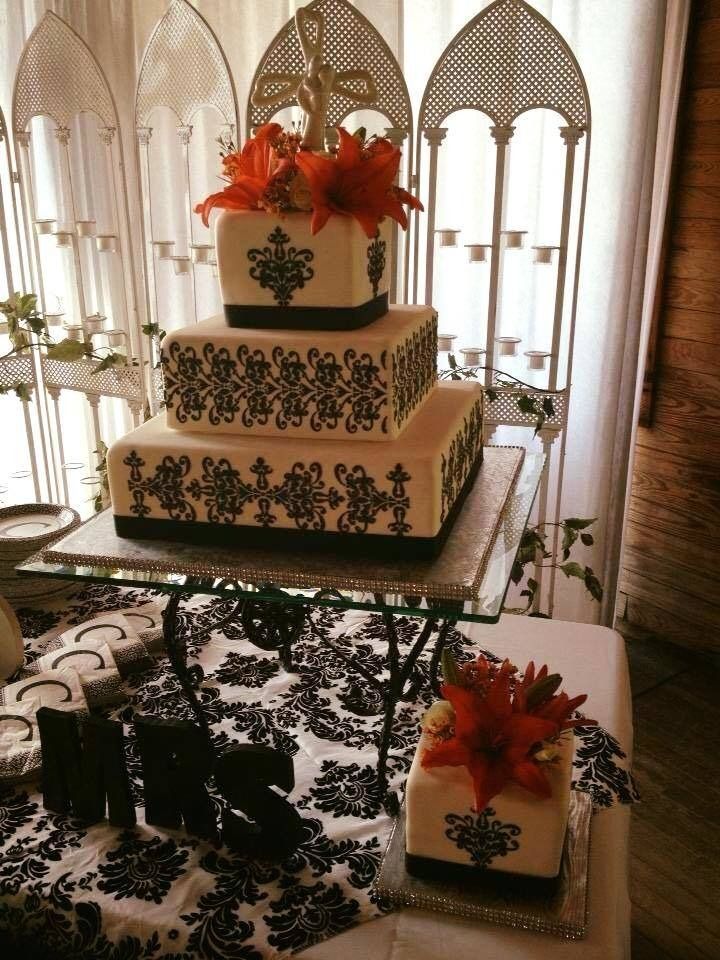 Tiered white cake with black floral accents and orange flowers on a decorated table in an elegant room