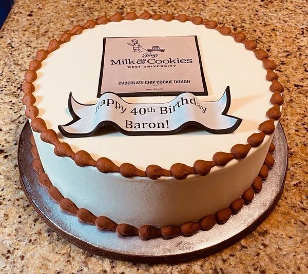 White frosted birthday cake with brown piping and a topper reading “Happy 40th Birthday Baron!”