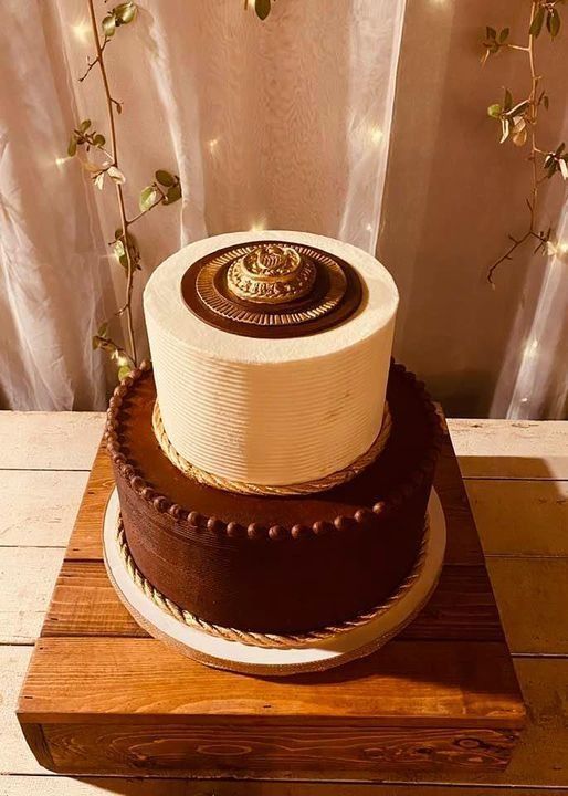 Two-tier chocolate and cream cake on a wooden board, topped with a chocolate medallion