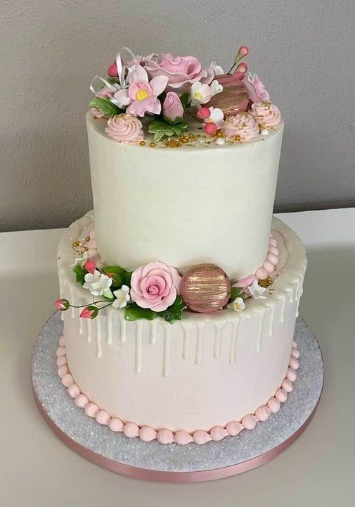 Two-tier white wedding cake with pink floral decorations and pearl accents on a silver board