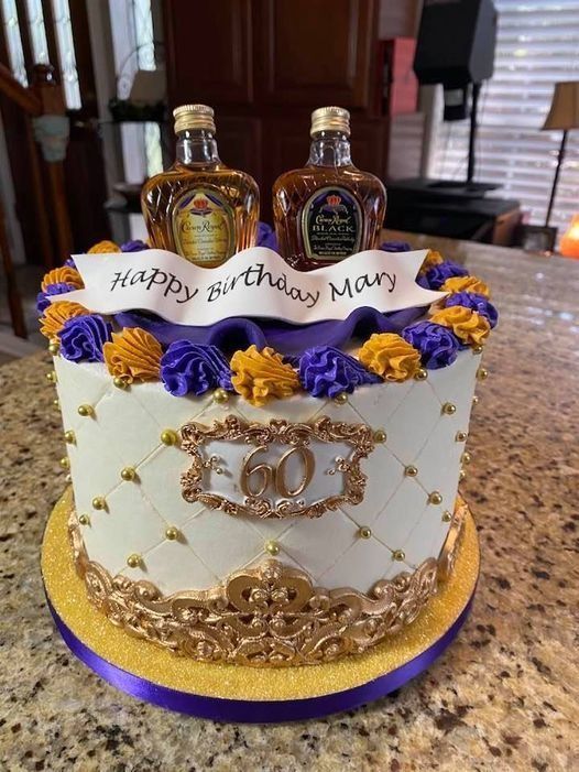 Happy birthday cake with purple and gold flowers, gold decor, and two liquor bottles on top