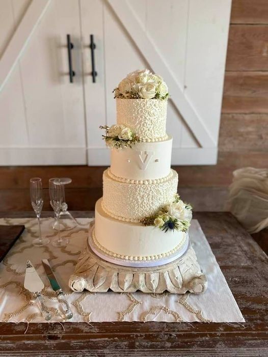 Five-tier white wedding cake with gold accents and flowers on a marble table in a rustic room