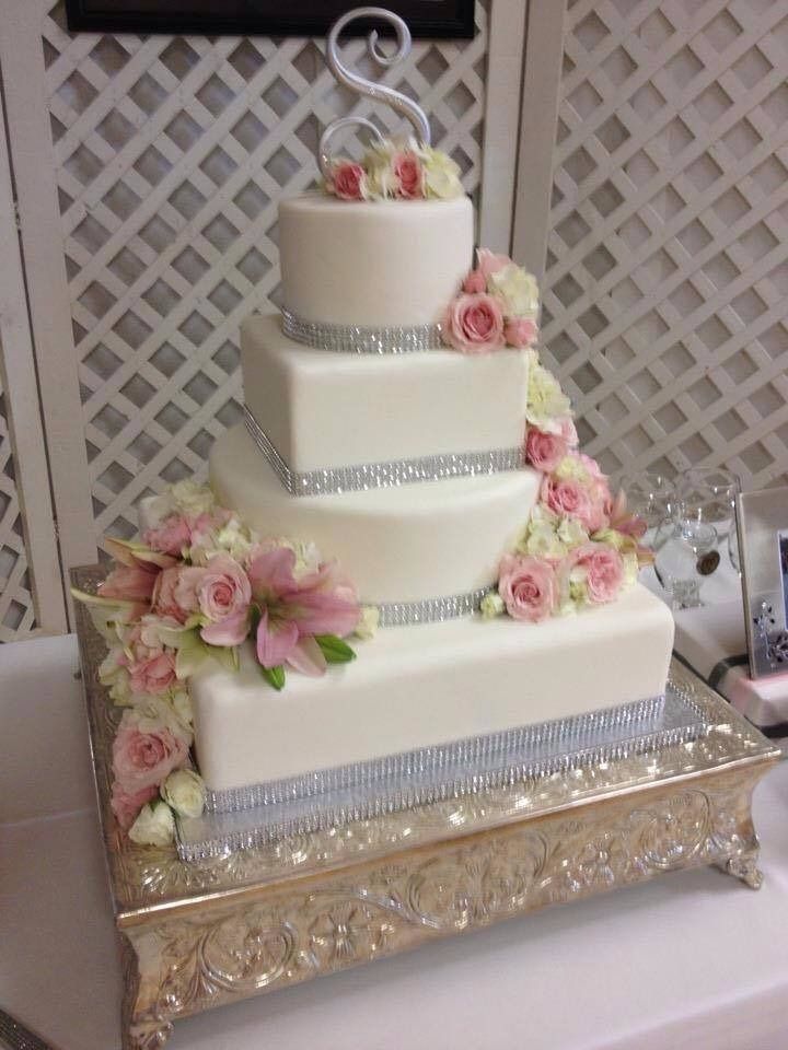 Tiered white wedding cake with pink roses and silver accents on a decorative gold table