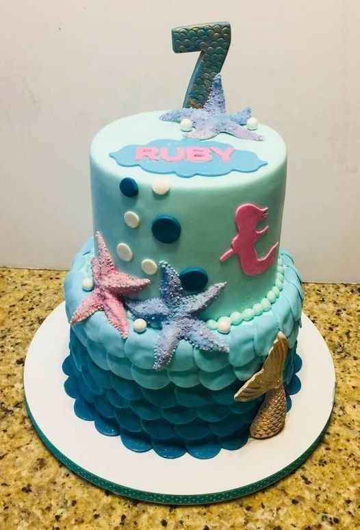 Blue mermaid-themed birthday cake with pink “Ruby” topper and glittery number 7 on top