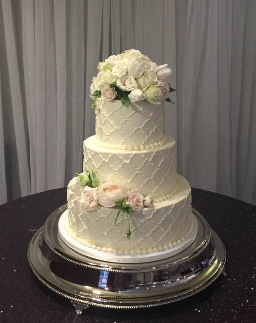 Three-tier white wedding cake with white flowers on a silver stand