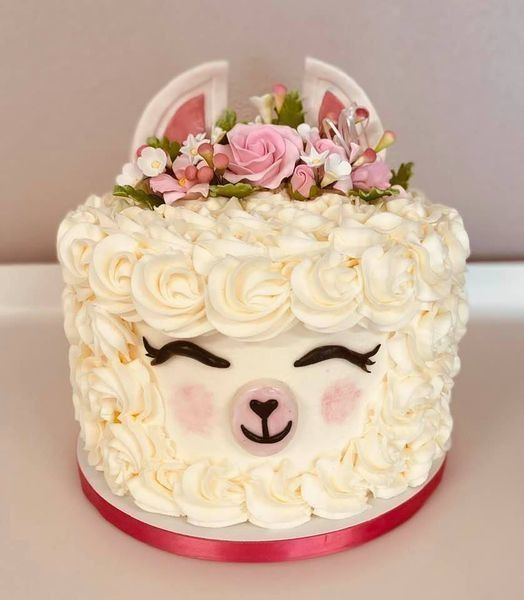 Cute lamb-shaped cake with white buttercream roses, pink flowers, and a pink ribbon trim