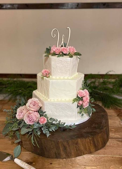 Three-tier white wedding cake with pink roses on a wooden stand