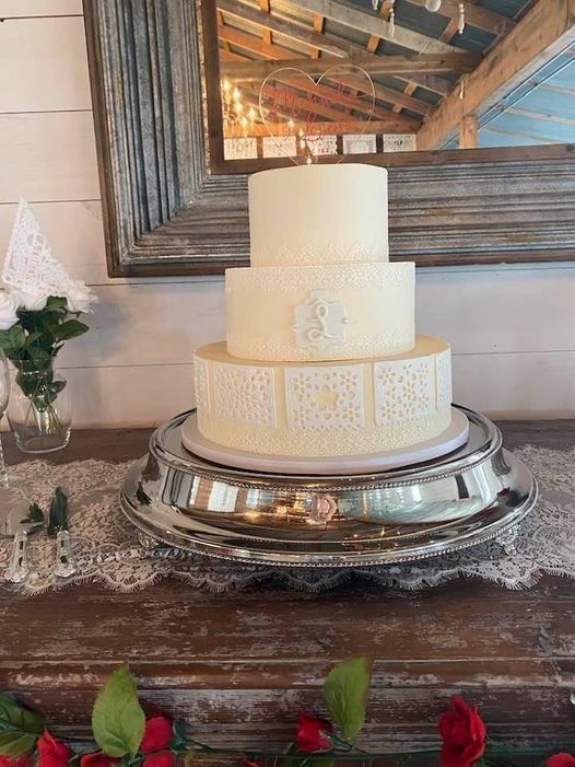 Three-tier white wedding cake on a silver stand, with floral decor on a rustic wooden table.