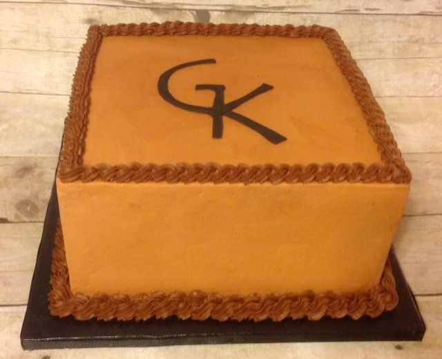 Square orange cake with brown frosting trim and black “GK” lettering on top