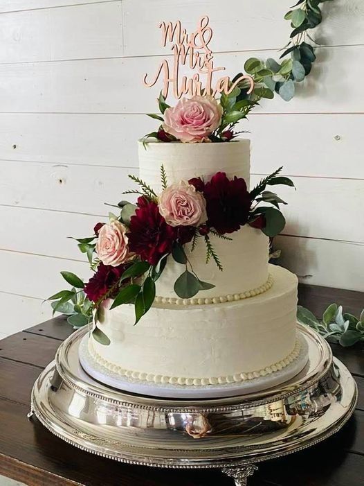 Three-tier white wedding cake with pink roses and greenery on a silver tray