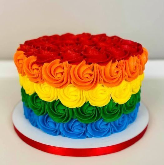 Rainbow-layered frosted cake with red, orange, yellow, green, and blue swirls on a white cake board