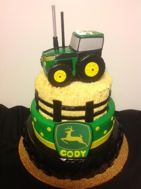 Green tractor cake topper on a yellow frosted cake with a “CODY” John Deere sign.
