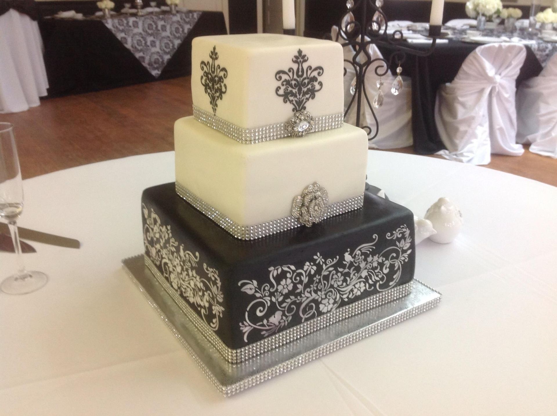 Three-tier black and white wedding cake with ornate silver patterns on a table