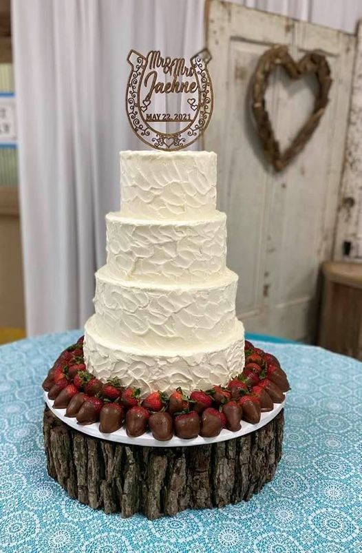 Four-tier white wedding cake topped with “Mr & Mrs,” surrounded by strawberries on a rustic wood stand