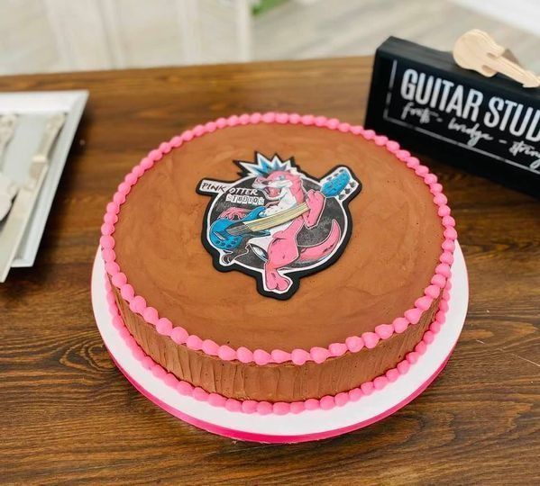 Chocolate cake with pink frosting trim and a colorful guitar topper on a wooden table