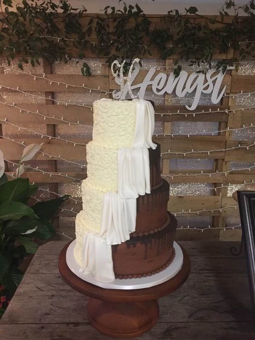 Two-tier chocolate cake with white cascading icing and a white name topper on a wooden stand