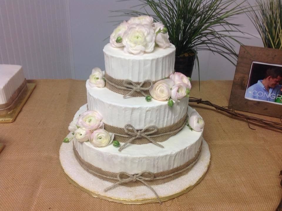 Three-tier white wedding cake with cream roses and ribbon on a table
