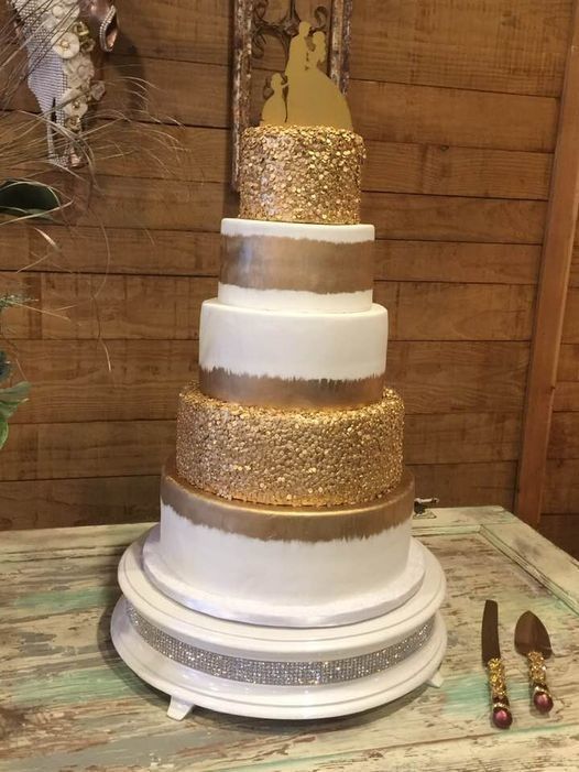 Five-tier white and gold wedding cake on a stand, with beaded decorations beside it.