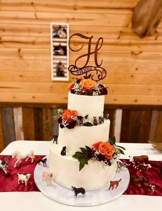 Three-tier white wedding cake with orange flowers and monogram topper on a decorated table