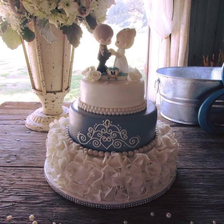 Decorative two-tier cake with white and blue icing and bride-and-groom topper on a rustic table