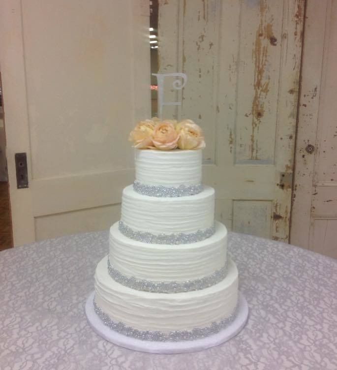 Four-tier white wedding cake with peach roses on top, displayed on a round table.
