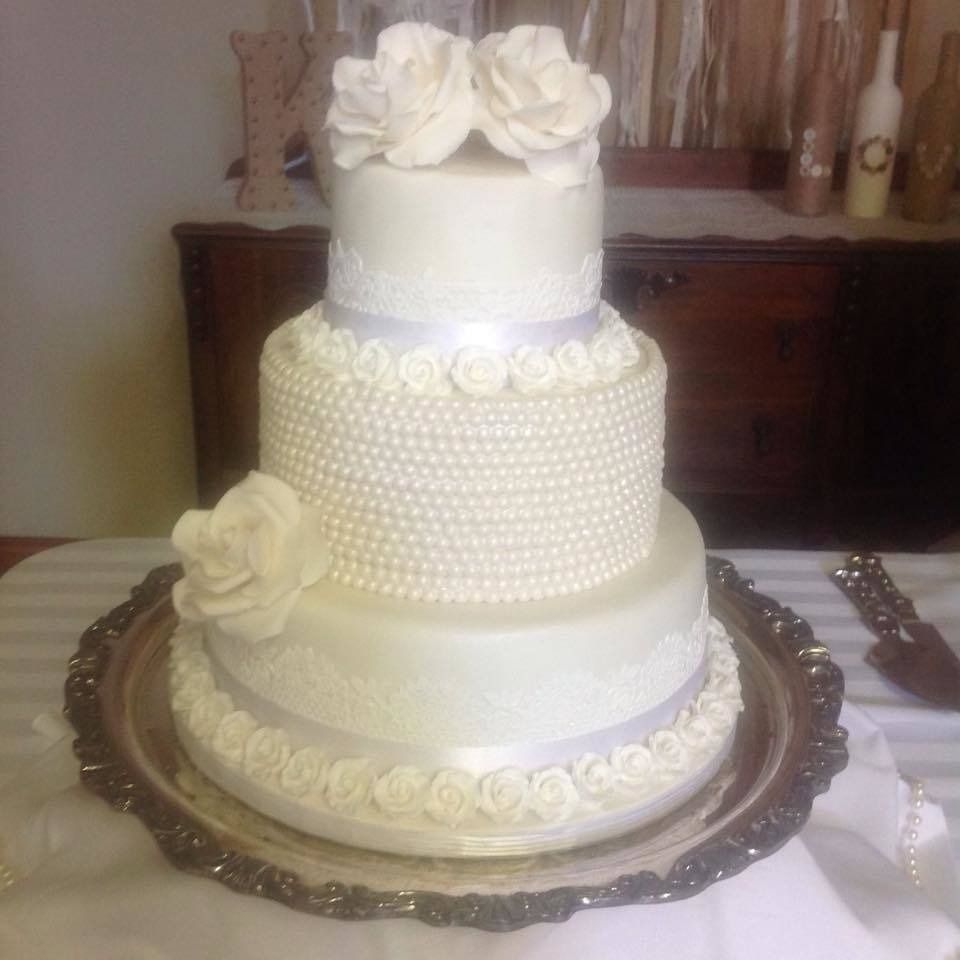 Three-tier white wedding cake with pearl-like icing and rose decorations on a silver tray