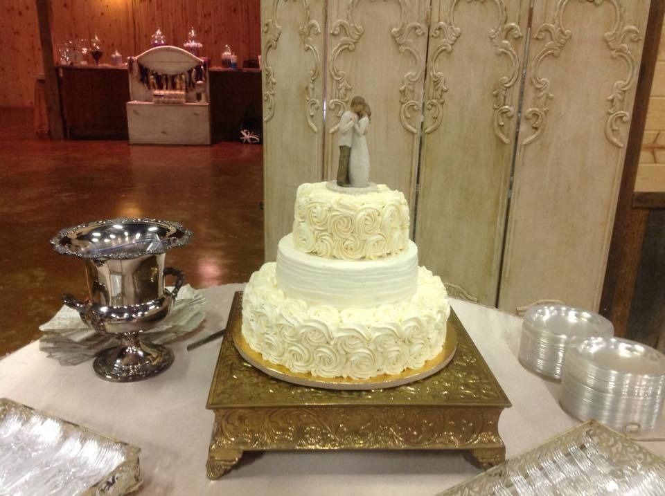 Decorated white tiered wedding cake on gold stand, with silver serving bowl beside it at a reception table