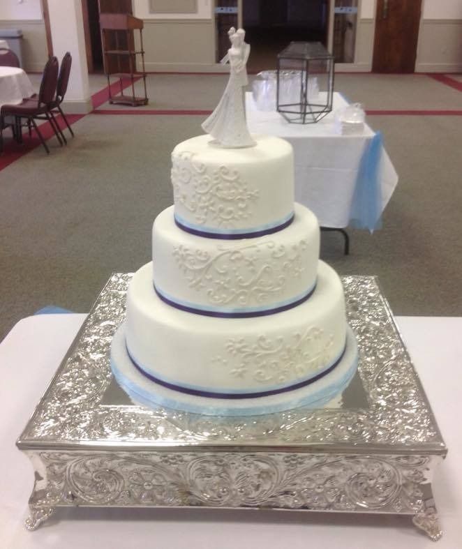 Three-tier white wedding cake with silver base and a bride topper on a decorated table.